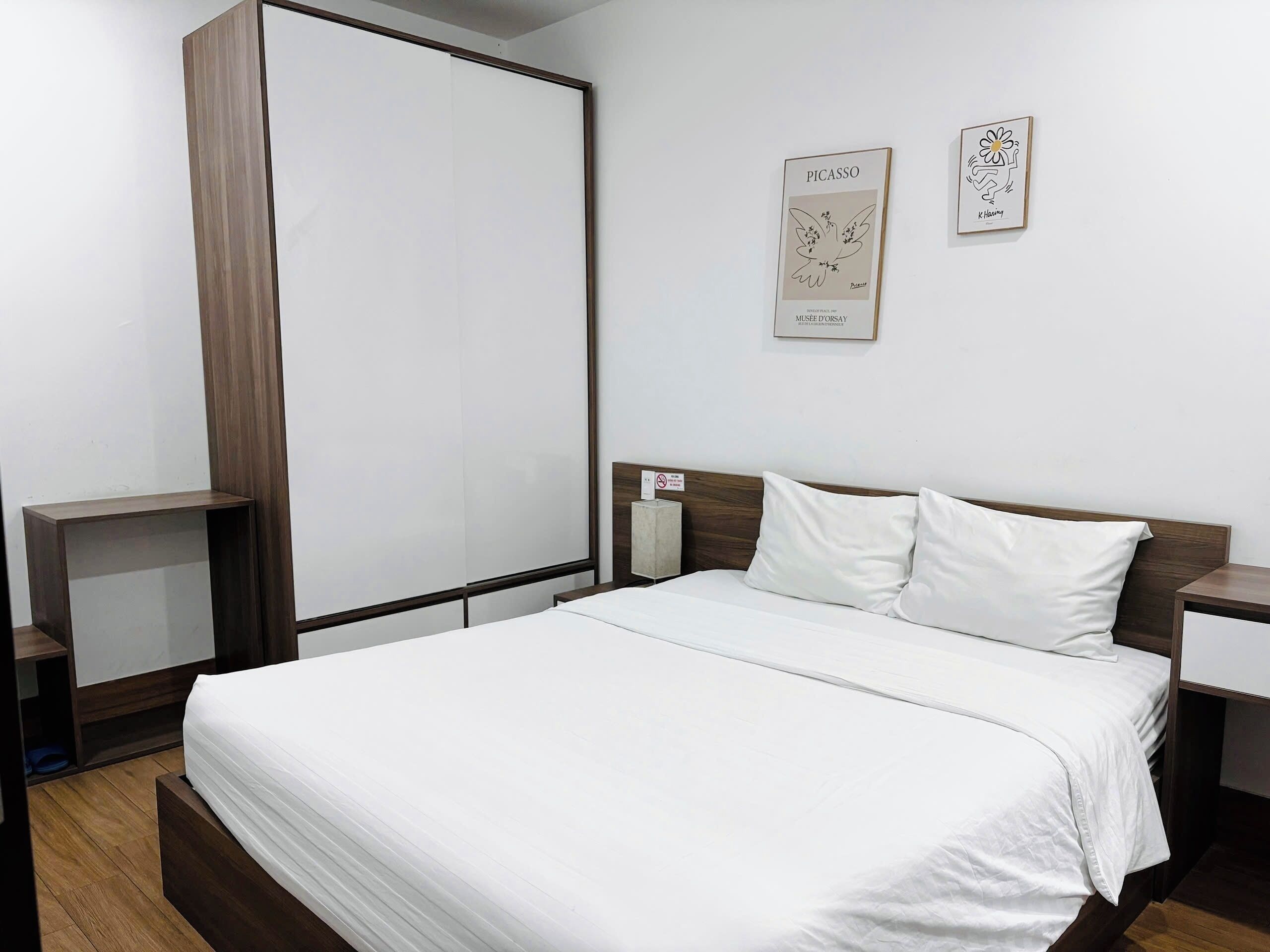 Ein Hotelzimmer mit einem großen Bett, einem Holzkopfstück, weißer Bettwäsche und zwei gerahmten Kunstwerken an der Wand.