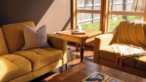Un soggiorno accogliente con un divano color senape, un tavolino da caffè con libri e un tavolino laterale in legno.