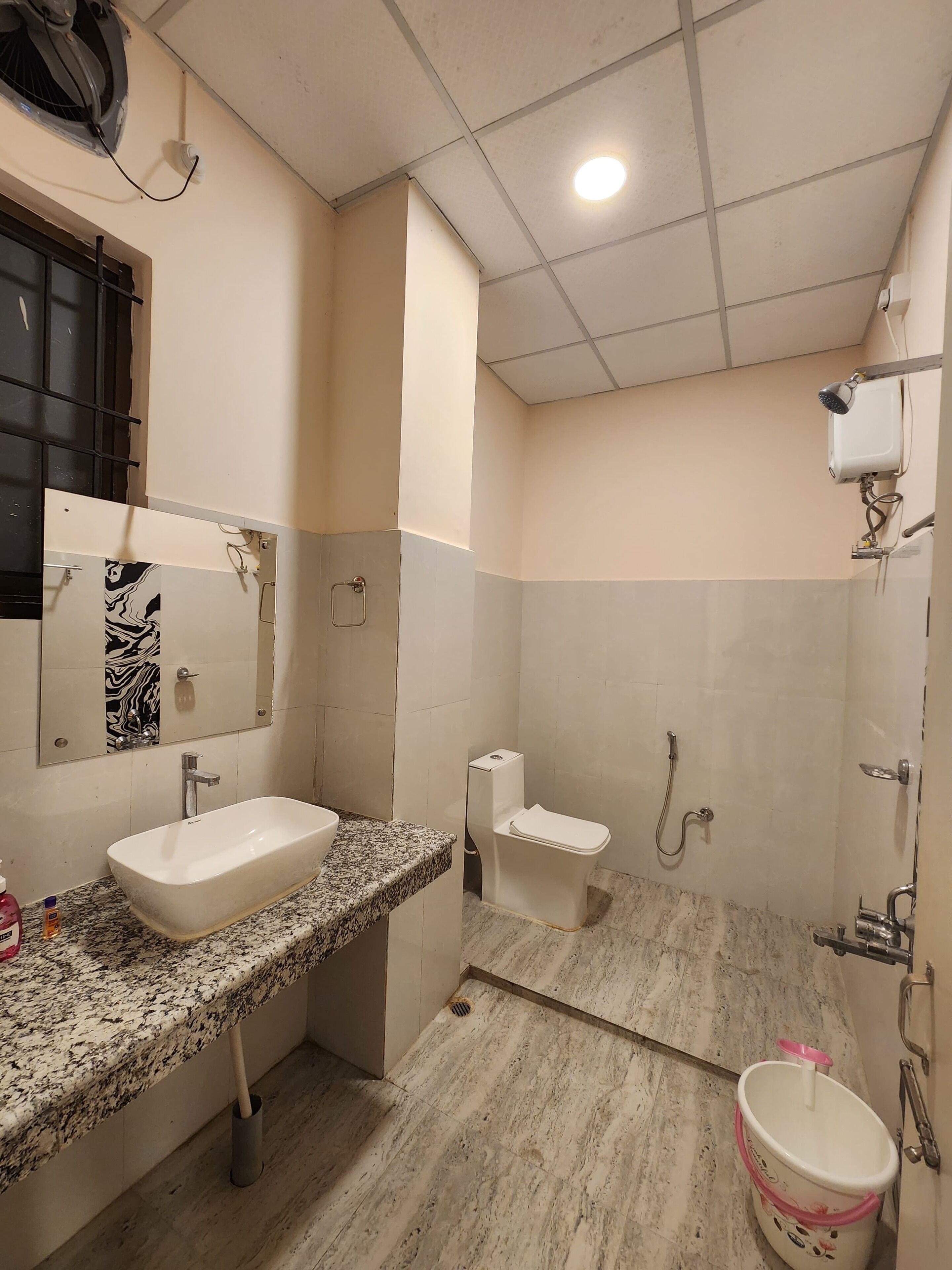 Une salle de bain équipée d’un lavabo, de toilettes, d’une douche et d’un seau.
