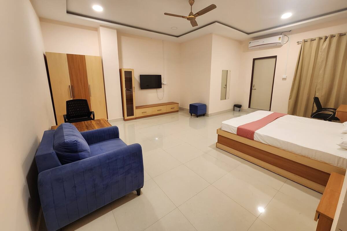 Quarto de hotel moderno com cama, sofá, televisão, ventoinha no teto e ar condicionado.
