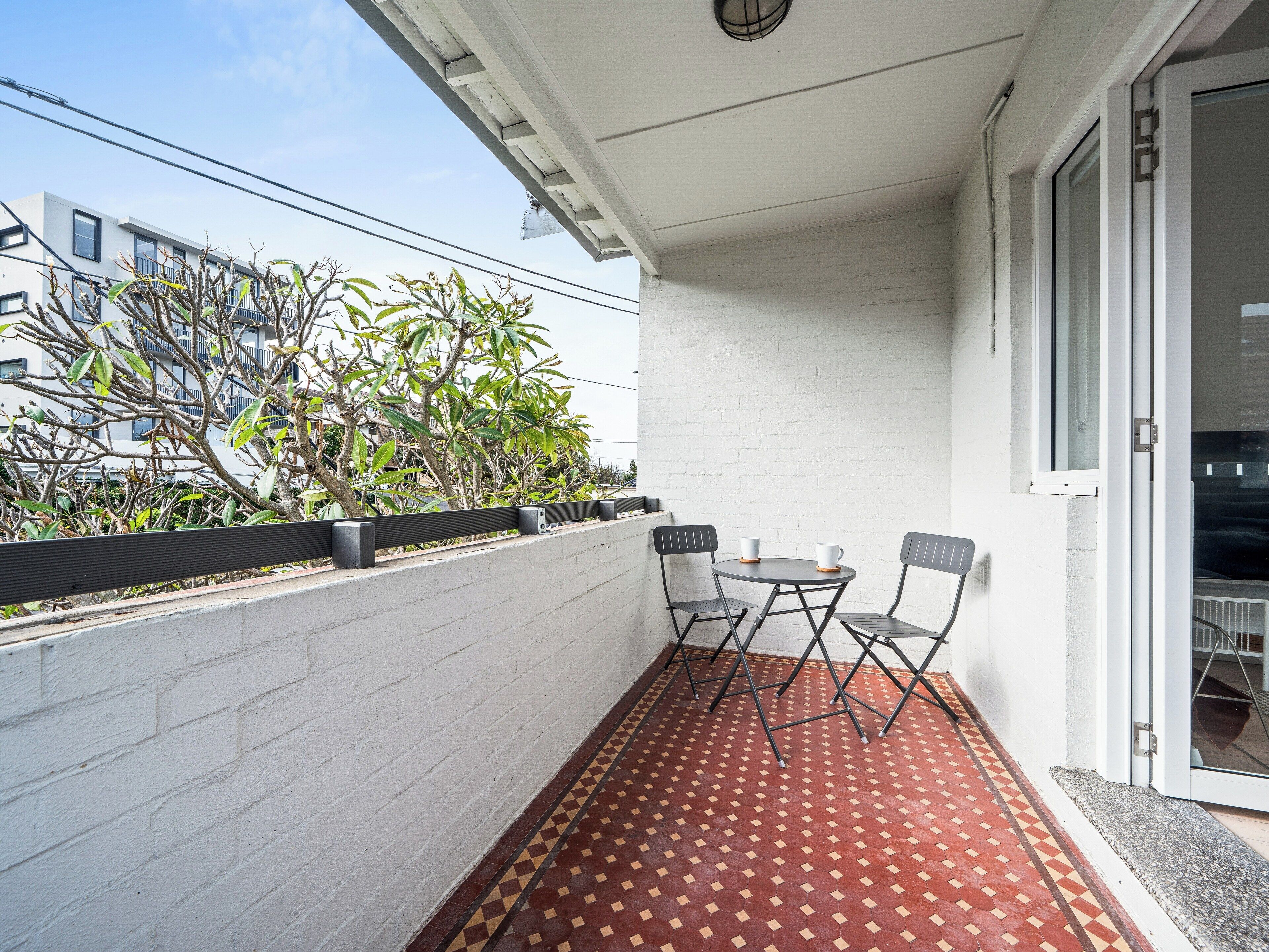 A balcony with a tiled floor, a small table with two chairs, and a white wall.