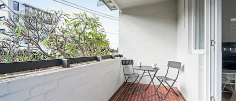 A balcony with a tiled floor, a small table with two chairs, and a white wall.