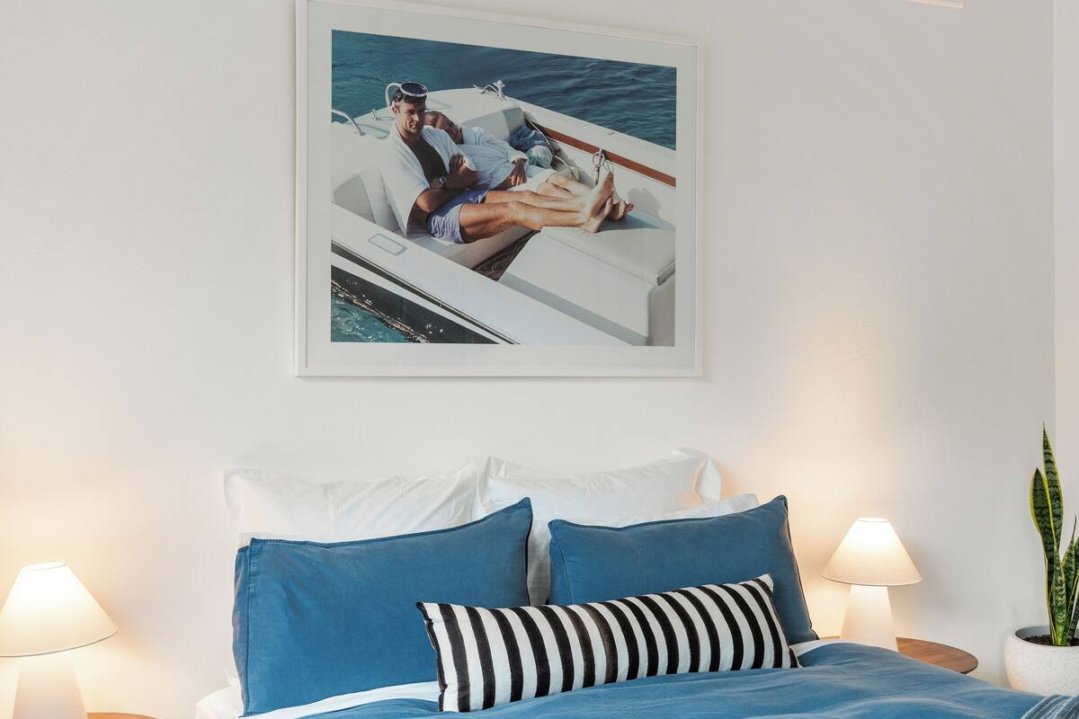 Un dormitorio con una cama, almohadas y un cuadro enmarcado de un barco en la pared.