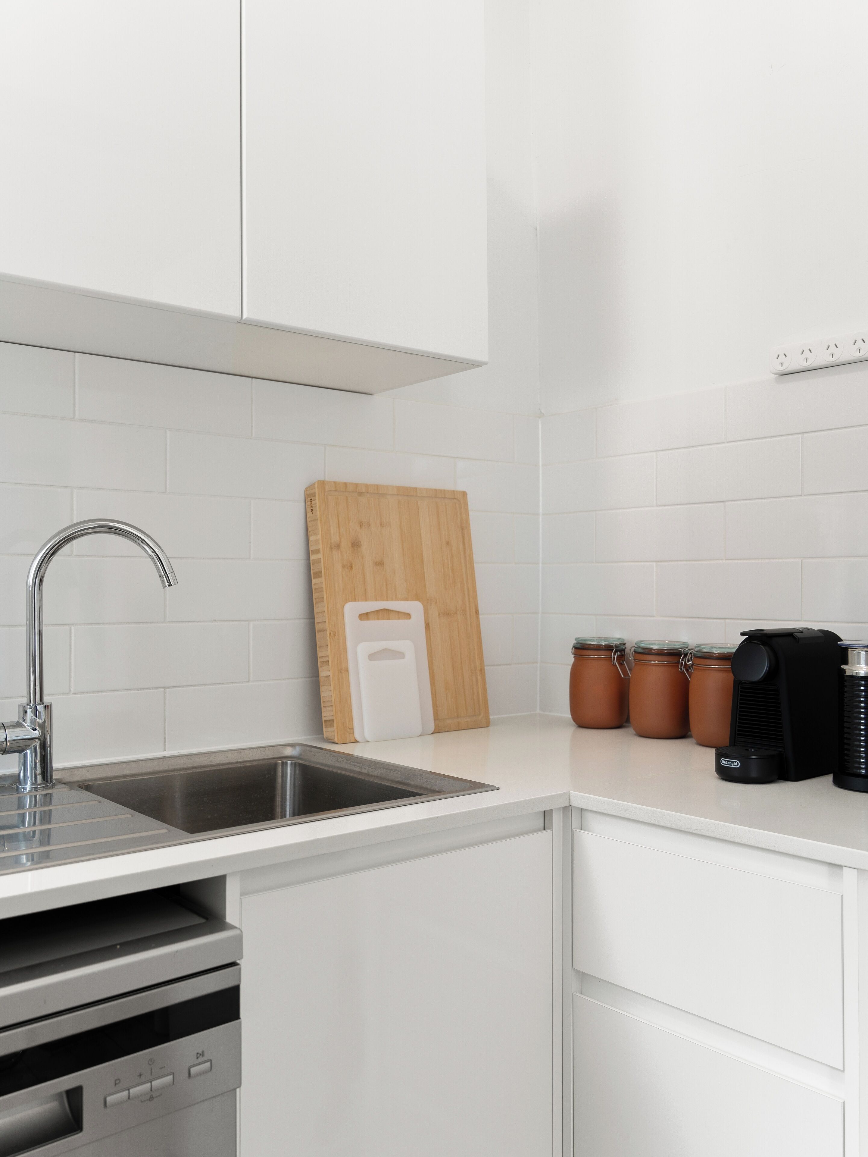 A kitchen with a stainless steel sink, a wooden cutting board, and three jars on the counter.