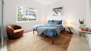 Une chambre à coucher comprenant un lit, une chaise, une fenêtre, un ventilateur de plafond et une petite table avec une lampe.