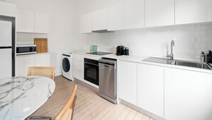 Une cuisine moderne avec des armoires blanches, un four encastré, un four à micro-ondes, une machine à café et un évier.