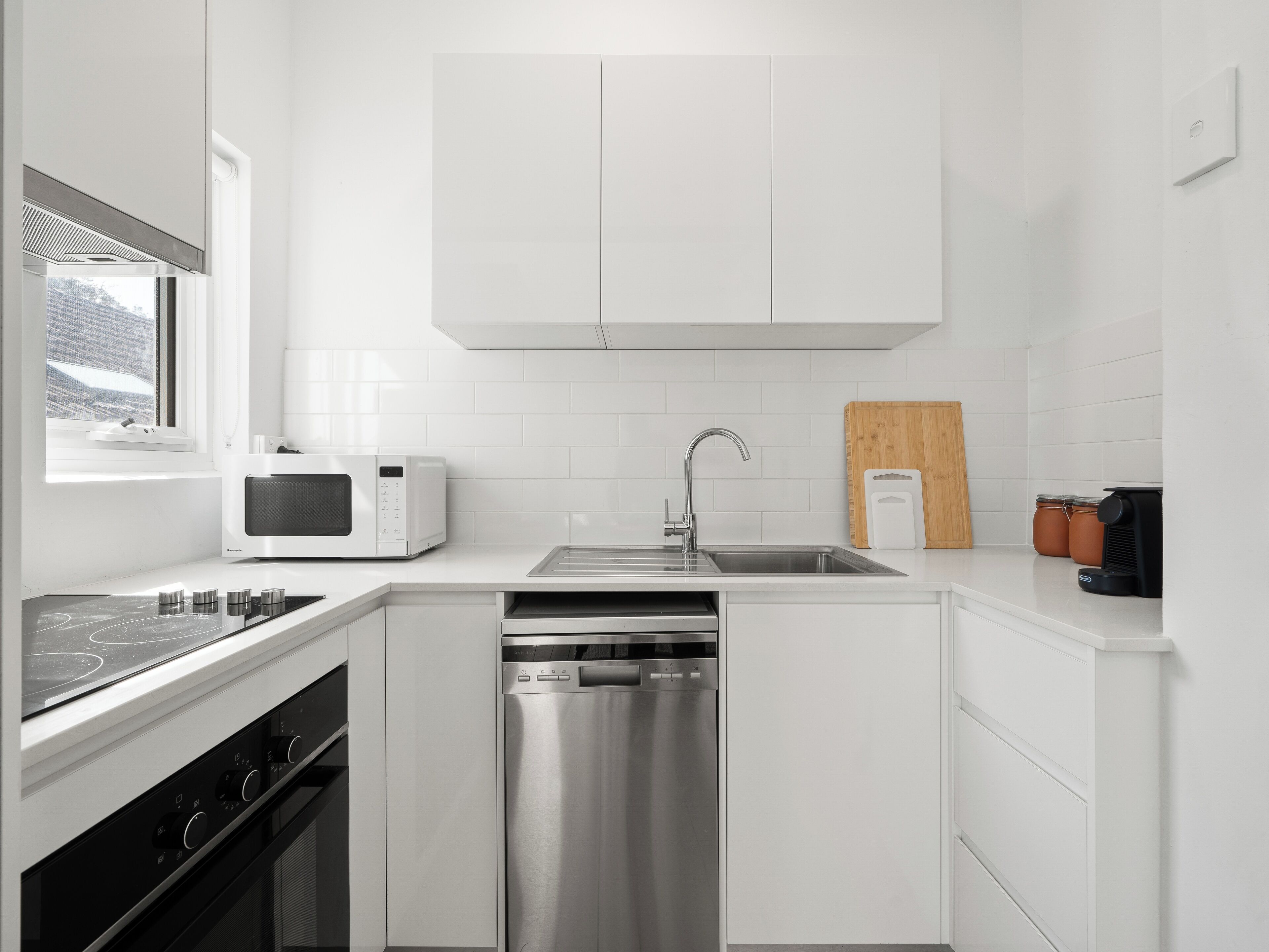 A modern kitchen with white cabinetry, a stainless steel dishwasher, a microwave, and a gas stove.