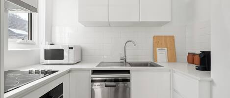A modern kitchen with white cabinetry, a stainless steel dishwasher, a microwave, and a gas stove.