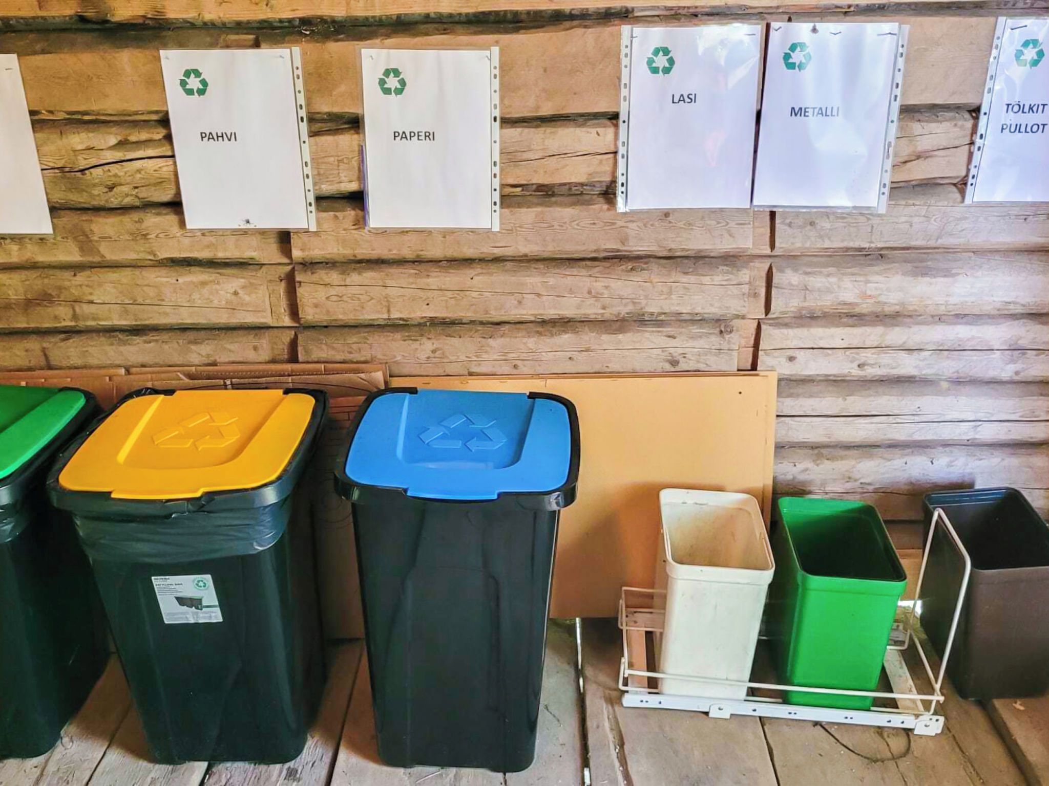 Eine Wertstoffsammelstelle mit beschrifteten Behältern für Papier, Plastik, Glas, Metall und sonstige Materialien.