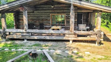 Une cabane rustique en rondins de bois, dotée d’une véranda, d’une table et de chaises.