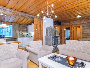 A cozy log cabin interior with a fireplace, two sofas, a dining table, and a kitchen area.