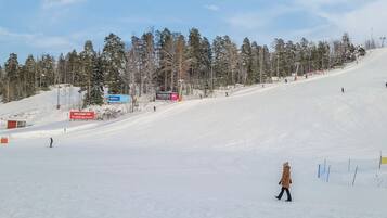 Pista de esquí nevada con una persona caminando, árboles y señalización.