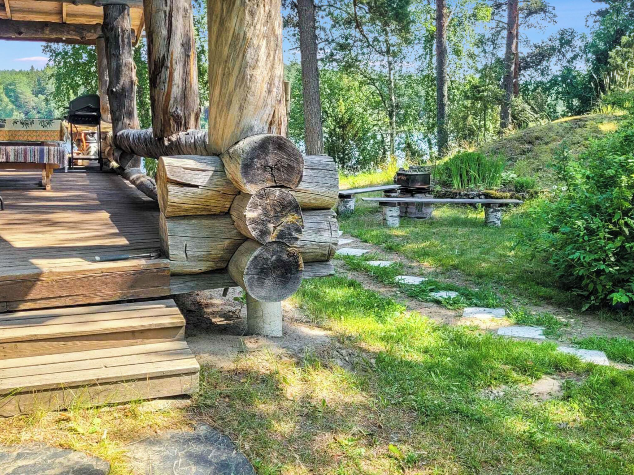 Una terraza de madera con un área de estar al aire libre de estilo rústico, una pila de leña y un sendero de piedra que lleva a una mesa de picnic.