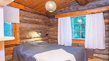 Habitación de cabaña de madera con una cama, lámpara colgante y ventana con cortinas.