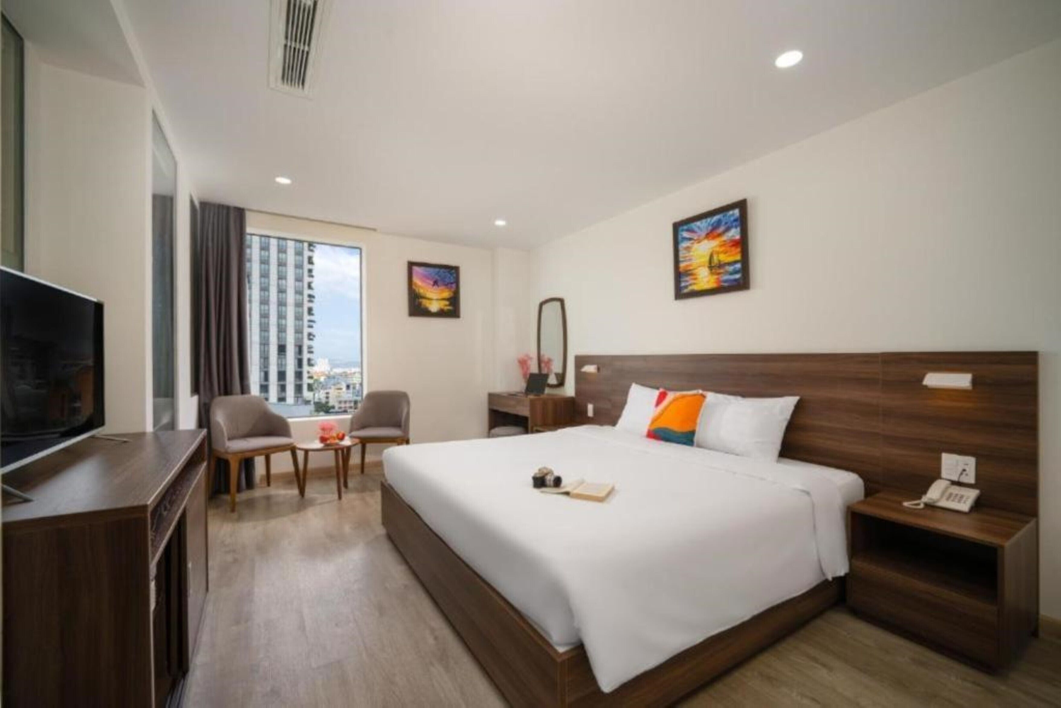 A hotel room with a large bed, a desk, a chair, a TV, and a city view.