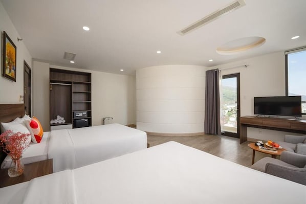 Habitación de hotel con dos camas, televisión, escritorio y balcón con vistas.