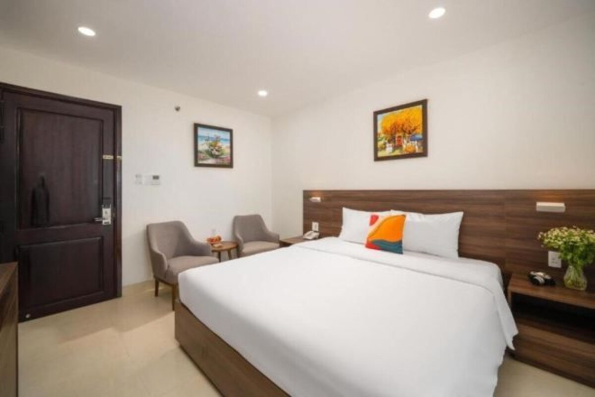 Hotelkamer met een groot bed, een houten hoofdbord, twee stoelen, een kleine tafel en een deur.