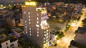 A multi-story hotel with a rooftop terrace, surrounded by a cityscape at night.