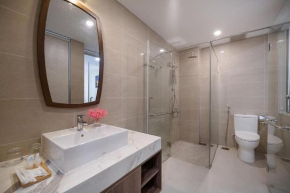 Een moderne badkamer met een grote spiegel, een witte wastafel, een douche met glazen wanden en een toilet.