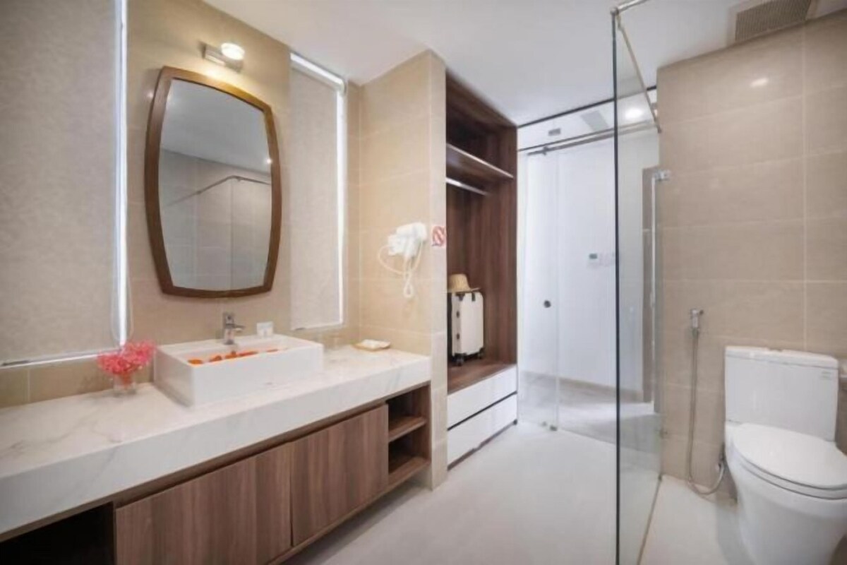 Une salle de bain moderne avec un grand miroir, un lavabo blanc, une zone douche et des toilettes.