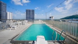 A rooftop pool with lounge chairs and a view of city buildings.