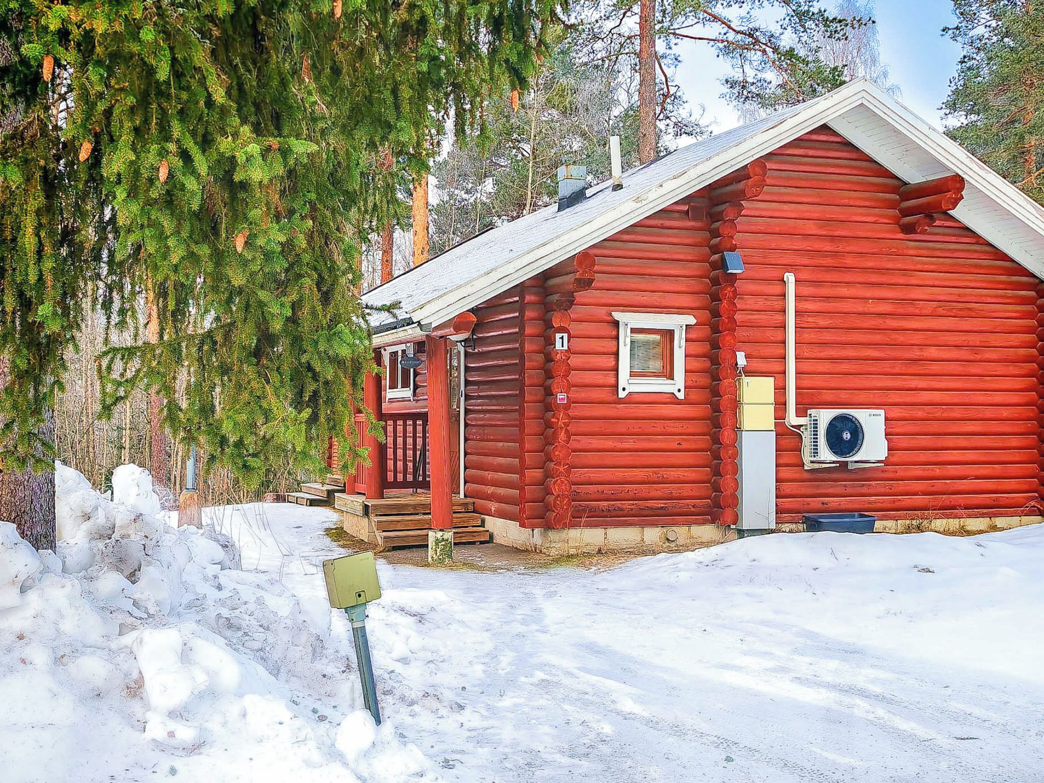 Eine rote Blockhütte mit einem Eingang, einer kleinen Veranda und einem Fenster.