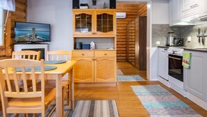 A cozy cabin interior with a wooden dining table, chairs, a TV, and a kitchen area with white cabinets and a stove. - Rustholli 1 by Interhome (Tampere)