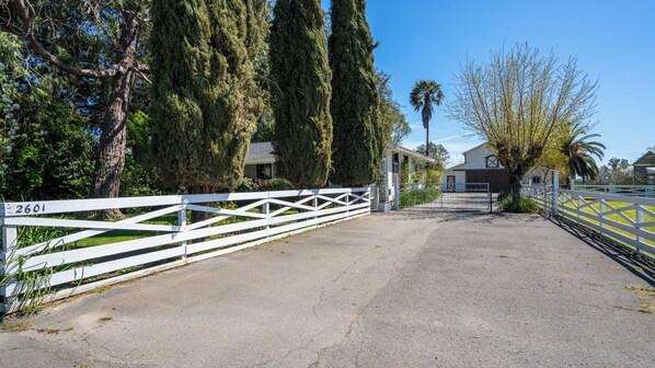 A gated driveway leading to a residential area with tall trees and a clear sky.