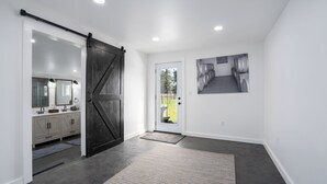 Een modern interieur met een schuifdeur in boerderijstijl naar een badkamer, een deur met uitzicht op vaten buiten, en een zwart-wit foto in een lijst aan de muur.