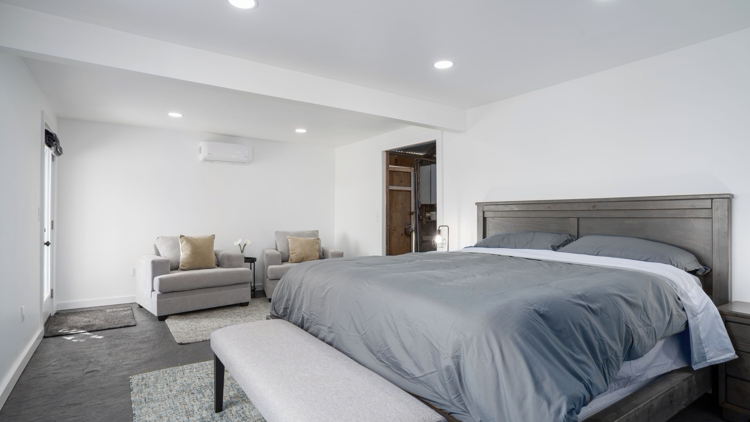 Un dormitorio moderno con una cama grande, un banco, dos sillones y una mesita.