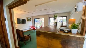 Une pièce spacieuse avec un plancher en bois, un tapis vert, une table à manger, des chaises rouges, une plante en pot et une caméra de surveillance.