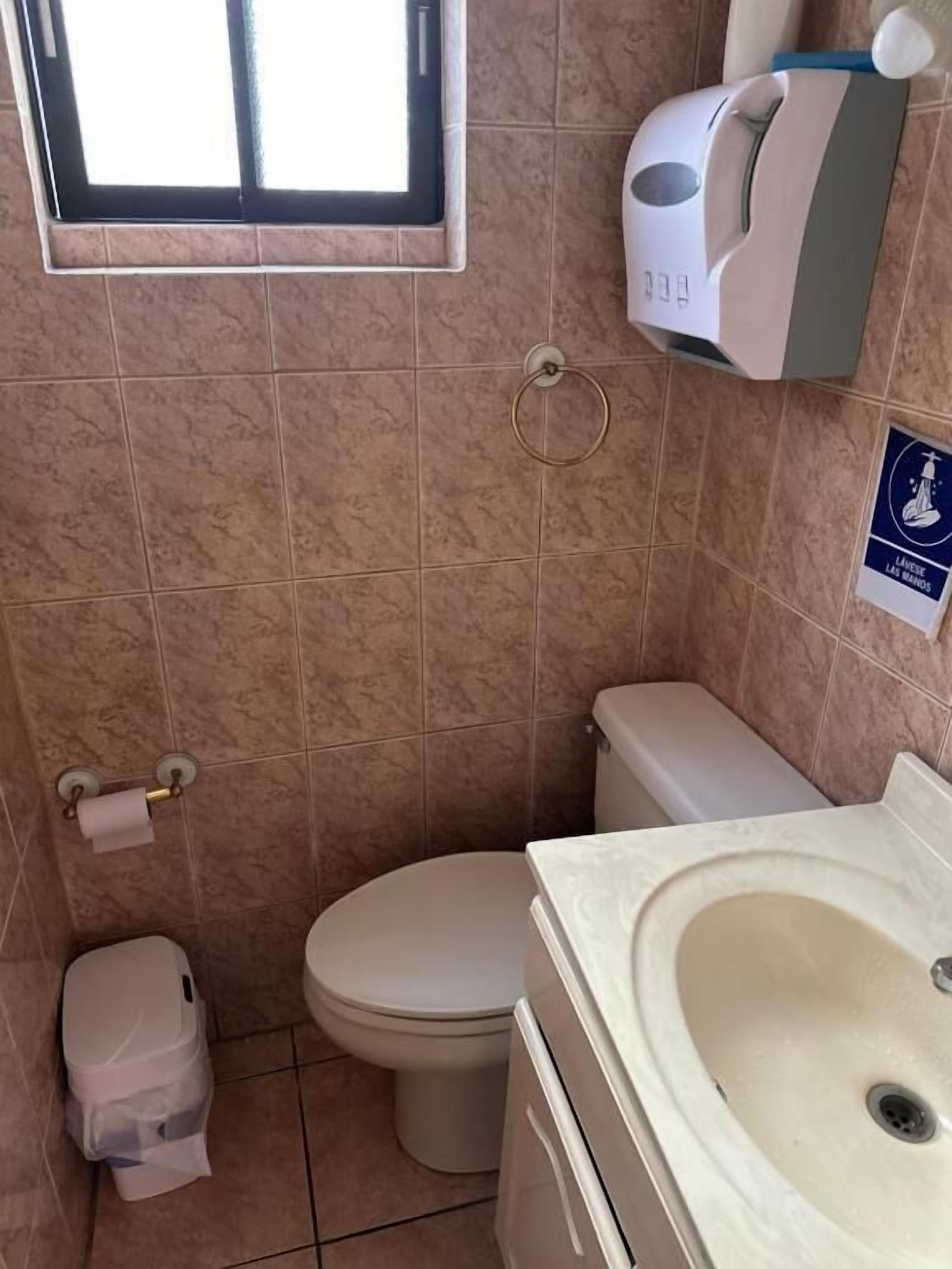 A bathroom with a toilet, sink, and hand sanitizer dispenser.