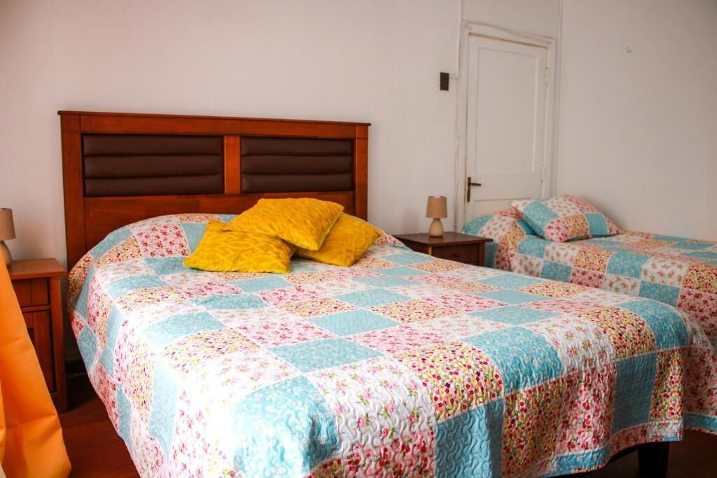A bedroom with two beds, each with a floral quilt, a wooden headboard, and bedside lamps.