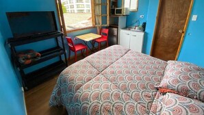 Une petite chambre comprenant un lit, un bureau, une chaise, un téléviseur et un coin cuisine.