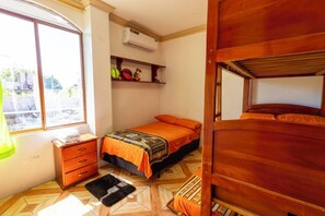 A compact bedroom with a bed, a dresser, a window, and a built-in shelf with decorative items.