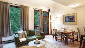 A living room with a sofa, a dining table with chairs, a lamp, and a painting on the wall.