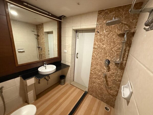 A bathroom with a sink, mirror, shower, and tiled walls. - MW HOTEL (Guwahati)