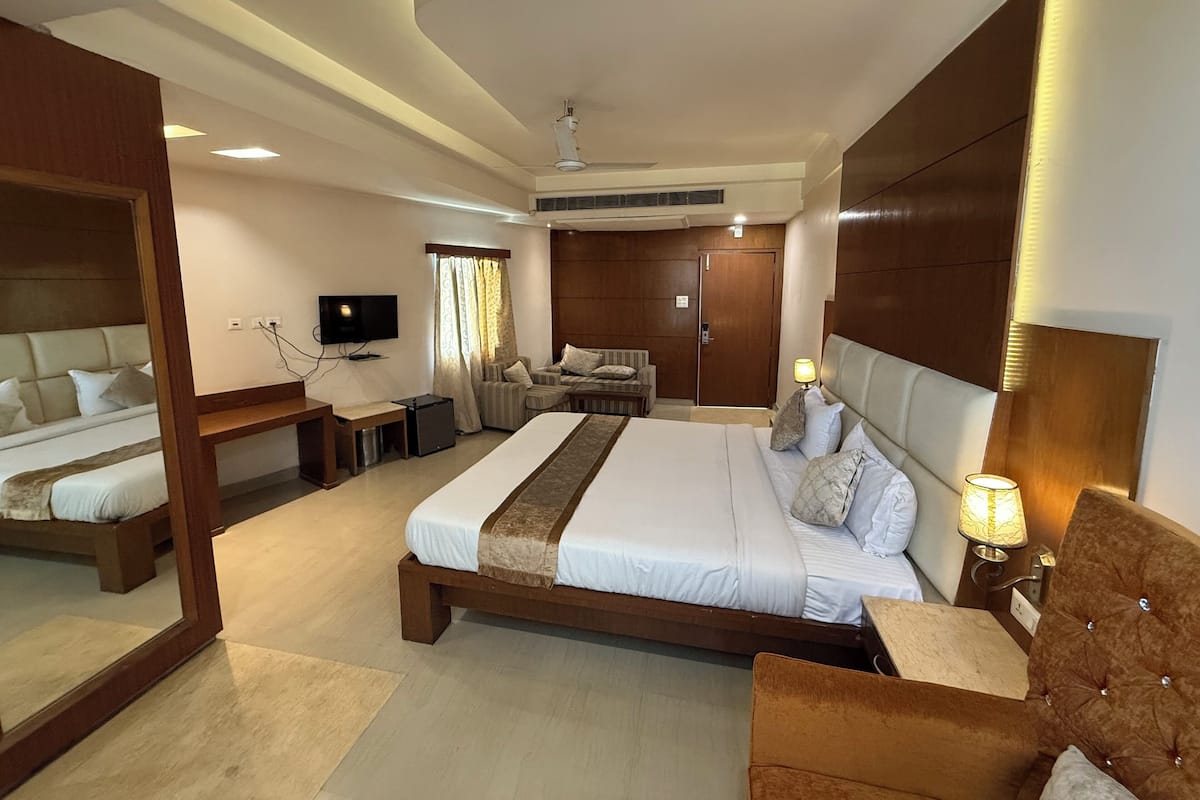 A spacious hotel room with a large bed, a seating area with a sofa and armchairs, a television, and a door.