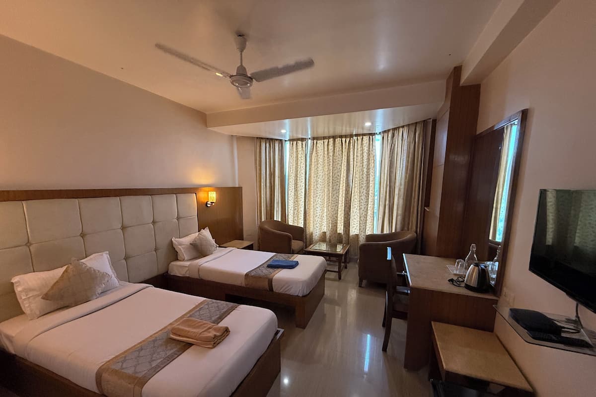 A hotel room with two beds, a desk, a chair, a television, and a ceiling fan.