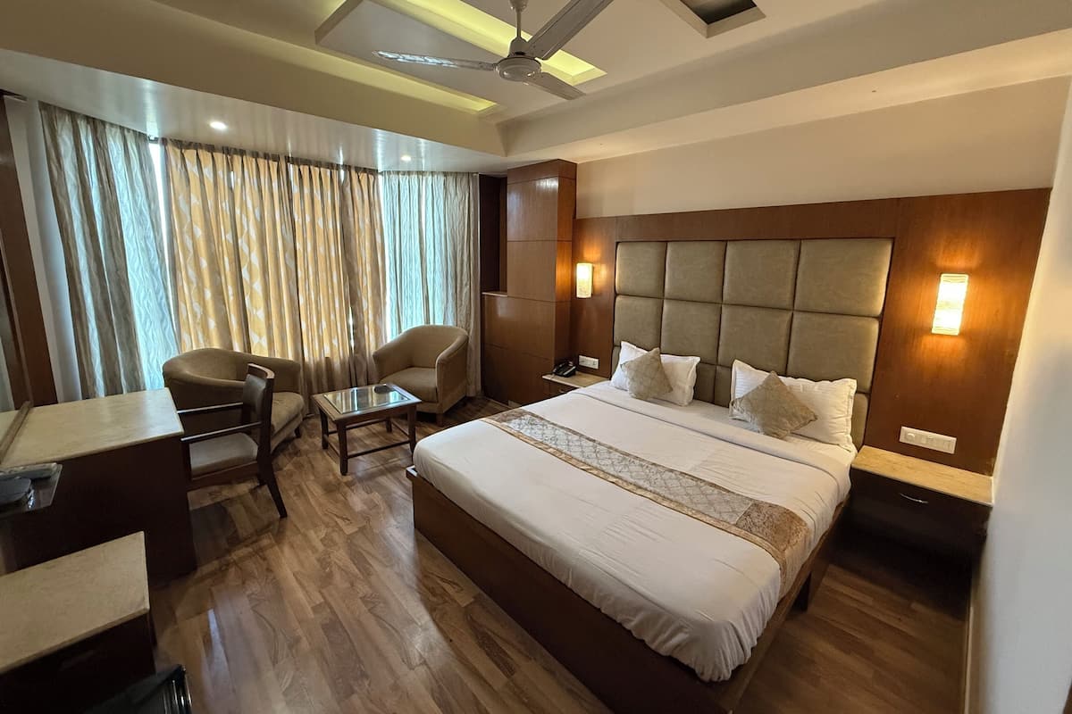 A hotel room with a large bed, a desk, a chair, a ceiling fan, and a window with curtains.