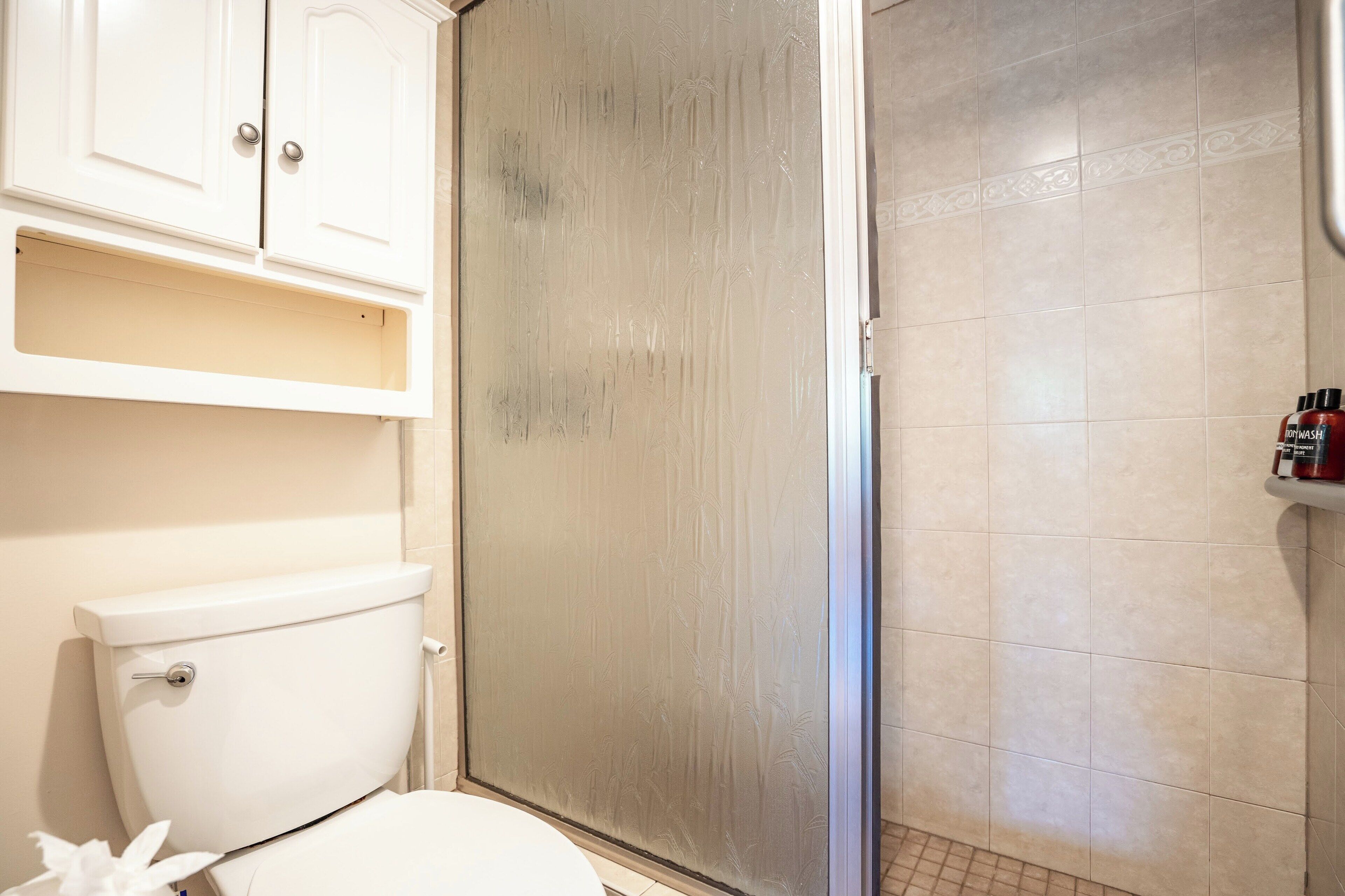 A bathroom with a toilet, a shower enclosure, and a cabinet above the toilet.