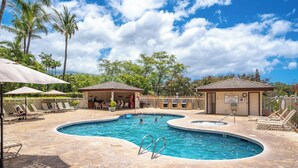 A pool area with lounge chairs, umbrellas, and a small building with a sign.