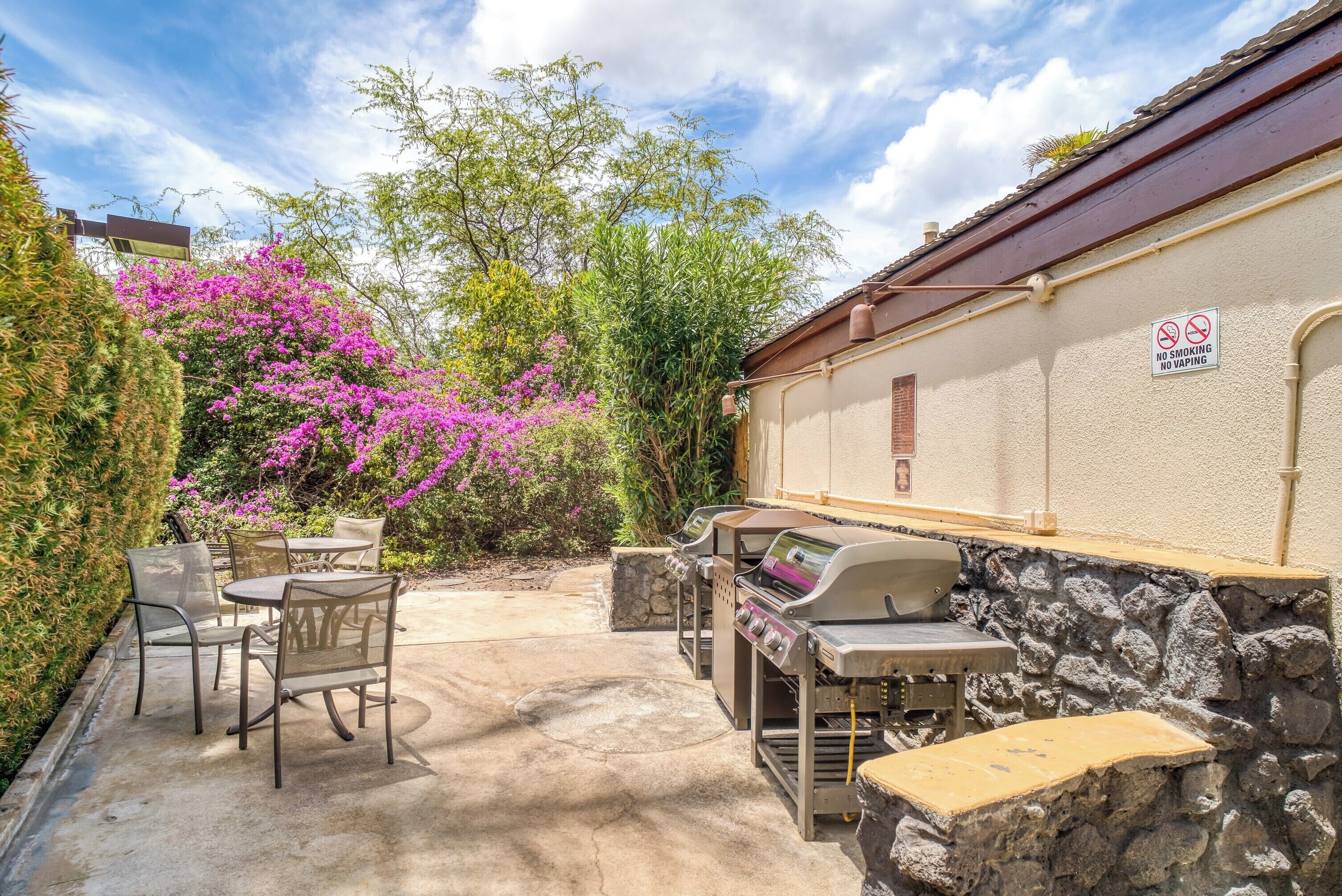 Une terrasse extérieure avec un barbecue, des chaises et un mur en pierre.