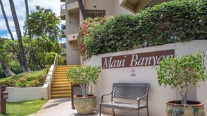 A hotel entrance with a sign reading "Maui Banyan," a bench, and potted plants.