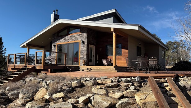 Una casa moderna con fachada de piedra, ventanas grandes y terraza de madera.