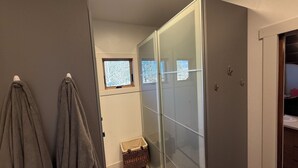Un baño con cabina de ducha de vidrio, toallero y ventana pequeña con vista a árboles.