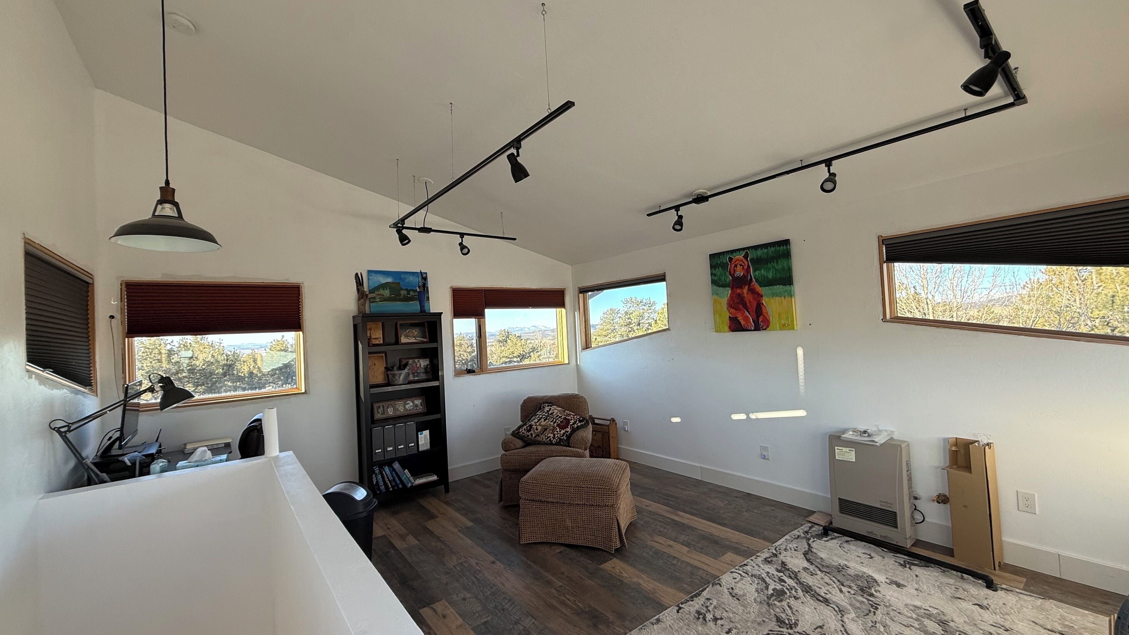 A spacious living room with a large window, a bookshelf, a chair, and a rug.