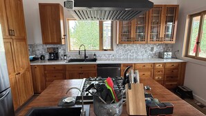 Una cocina moderna con armarios de madera, una isla central con utensilios de cocina, una cafetera y una ventana que proporciona luz natural.
