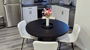 Une cuisine moderne avec des meubles blancs, des appareils en acier inoxydable et une table de salle à manger ronde entourée de chaises blanches.