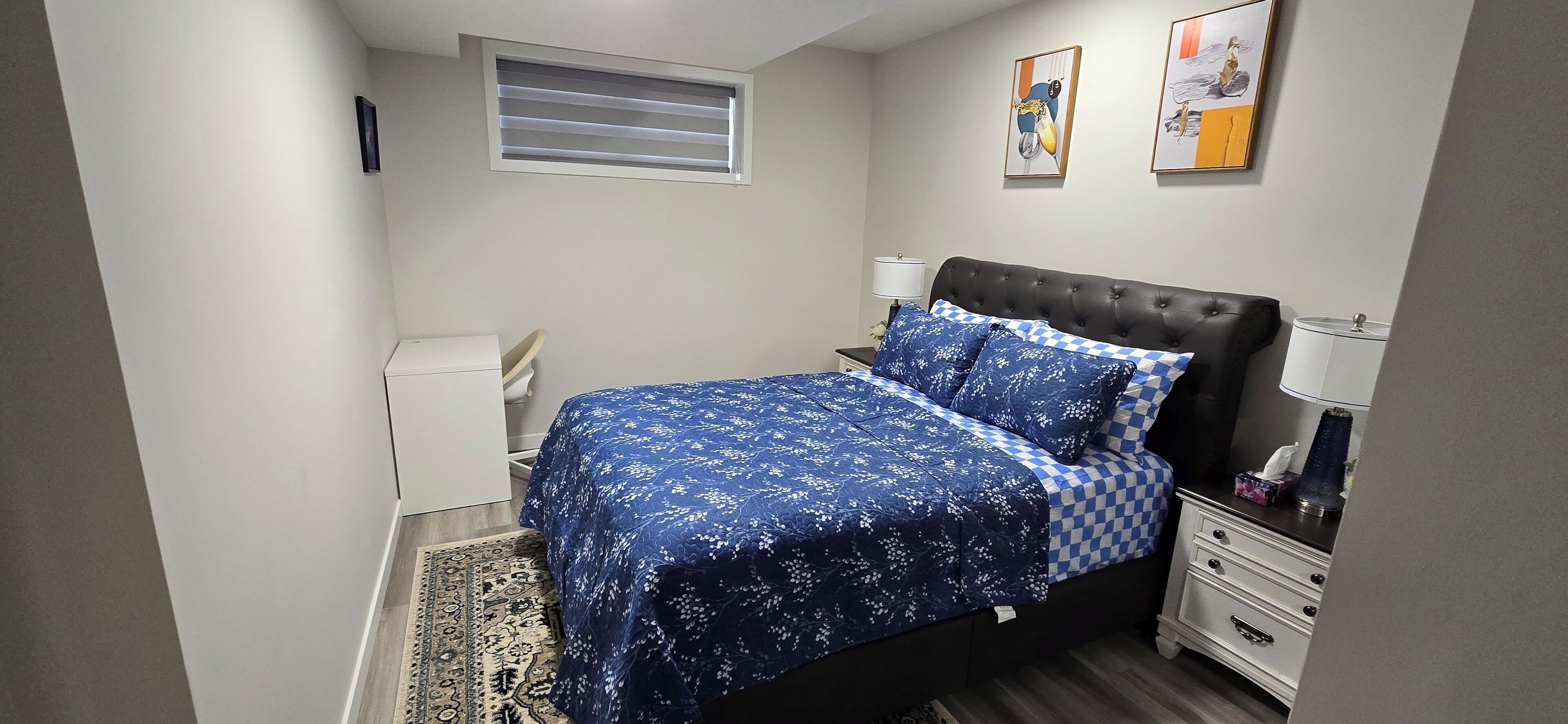 A bedroom with a bed, bedside tables, a lamp, a window, and artwork on the wall.